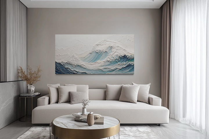 A large horizontal canvas of a textured teal ocean wave hangs above a modern neutral sofa.