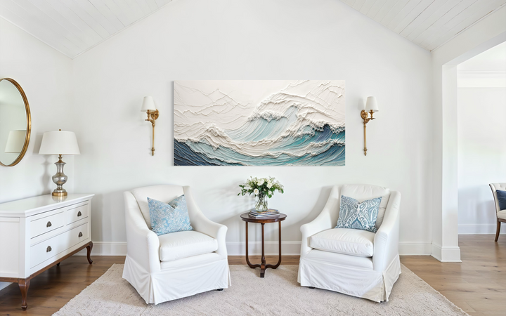 Textured 3D teal ocean wave canvas art centered above two white armchairs in a bright living room.
