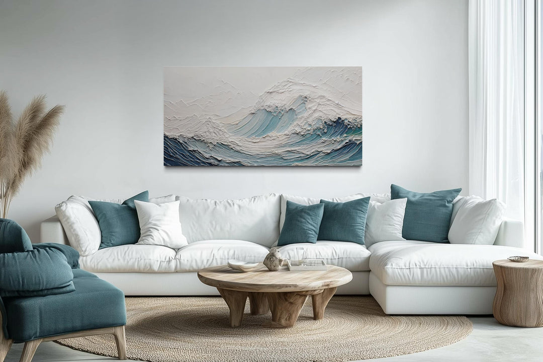 A large horizontal canvas of a textured 3D teal ocean wave hangs above a modern white sectional sofa.
