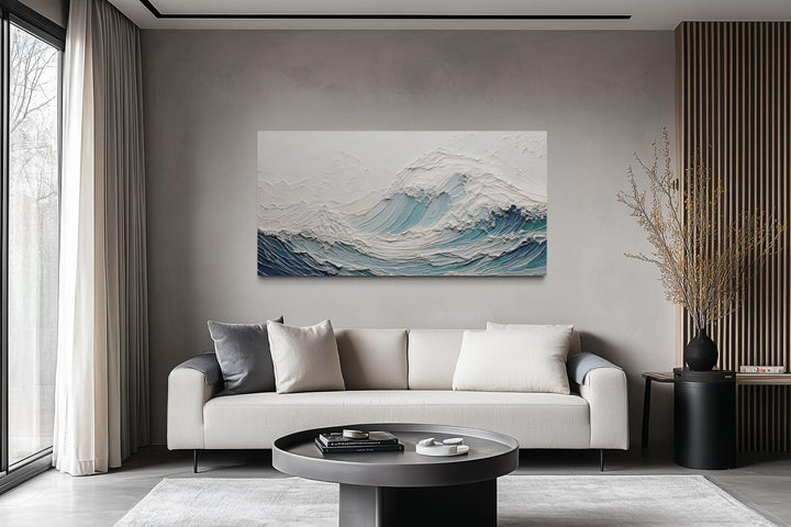 A large horizontal canvas of a textured teal ocean wave hangs above a modern sofa in a neutral room.