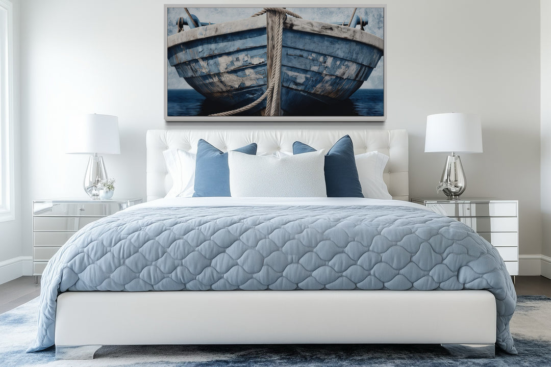 Old blue and white rustic boat nautical framed canvas wall art above a bed in a beach house bedroom.