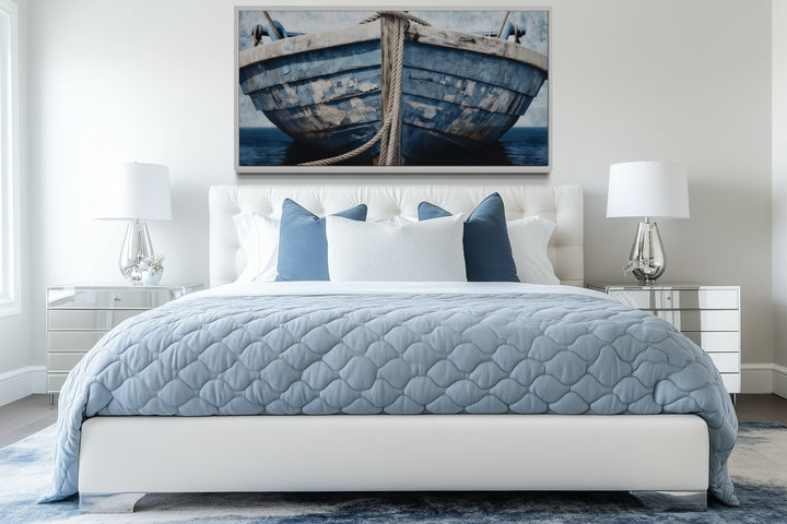 Old blue and white rustic boat nautical framed canvas wall art above a bed in a beach house bedroom.