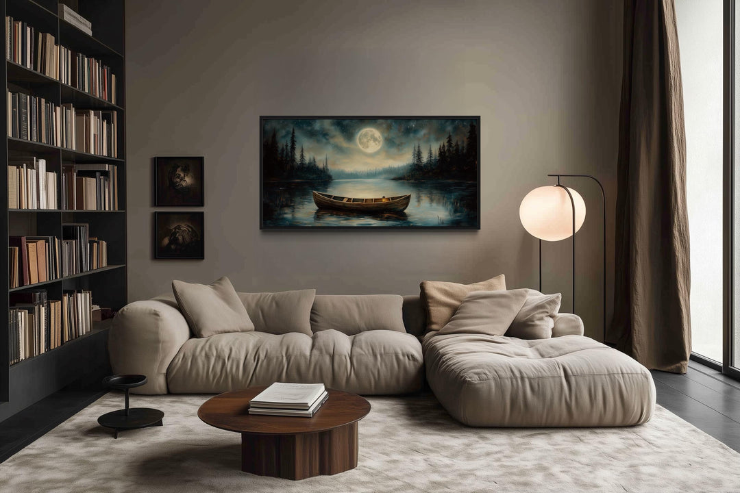 Old boat in the lake and moon at night framed canvas wall art above a beige sofa in a living room.