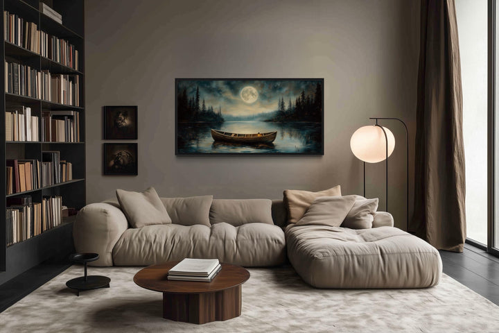 Old boat in the lake and moon at night framed canvas wall art above a beige sofa in a living room.