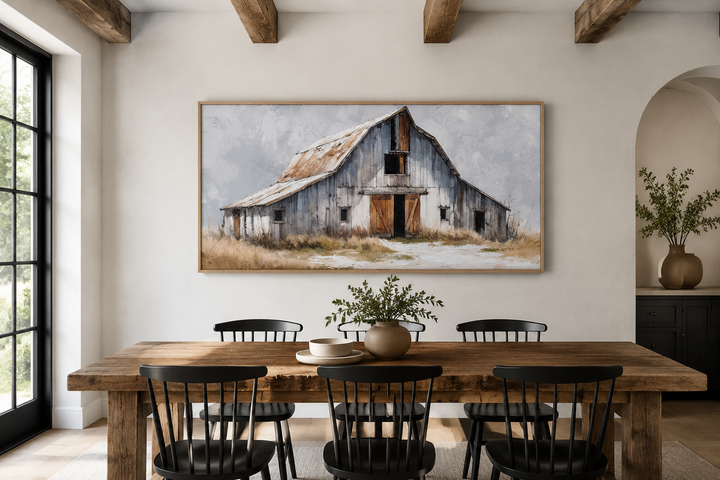 Rustic canvas wall art of an old grey barn above a wooden dining table with black chairs.
