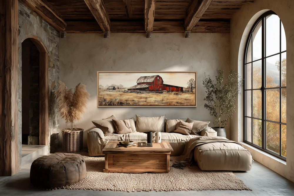 Horizontal framed canvas wall art of an old red barn in a rustic landscape above a beige sofa.