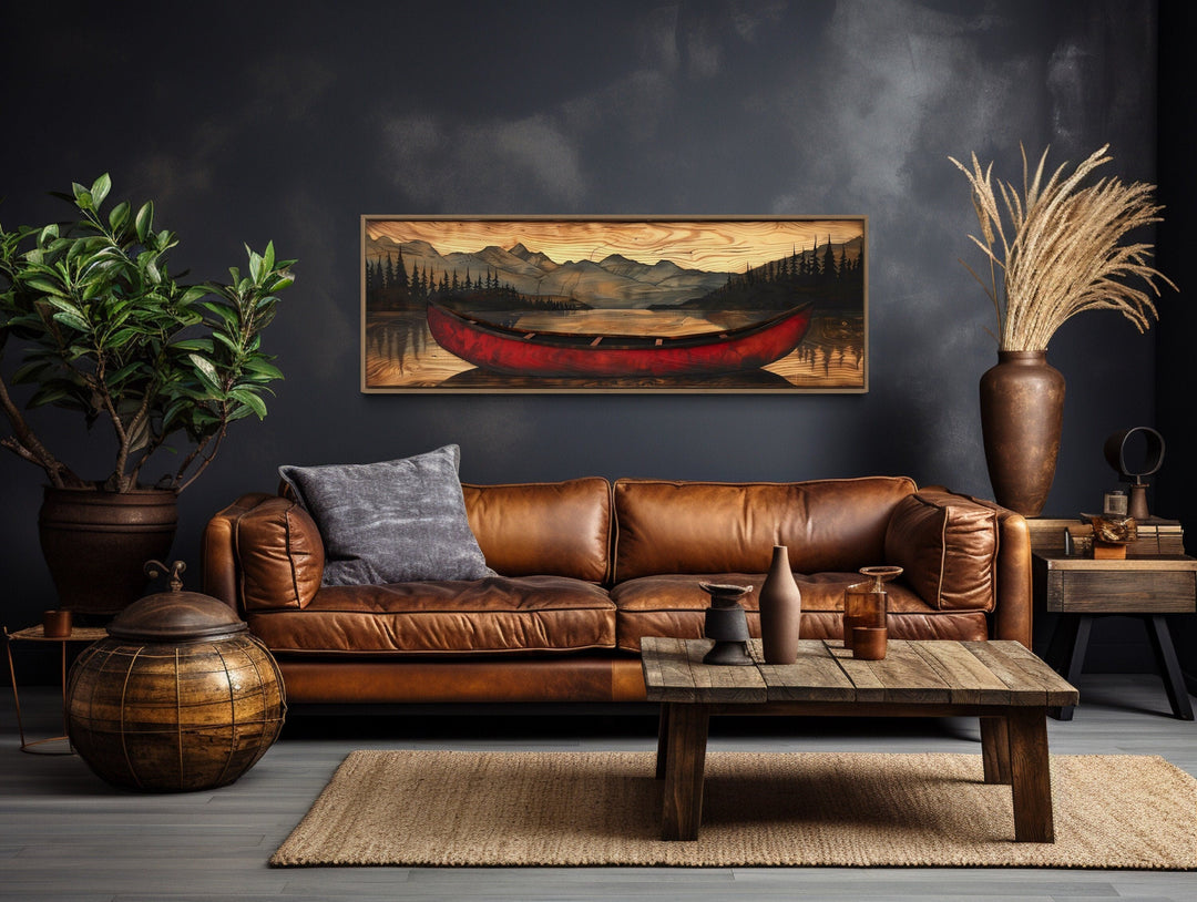 Long horizontal framed canvas wall art of a red canoe painted on wood above a leather sofa.