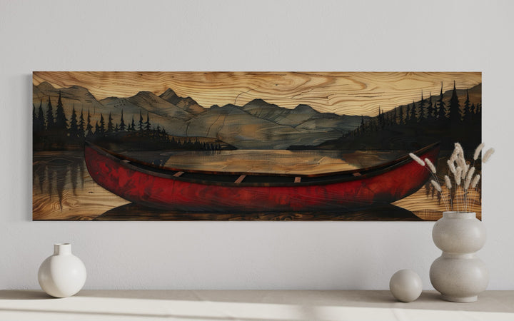 Long horizontal wall art of a red canoe on a lake with mountains painted on a wood grain background.