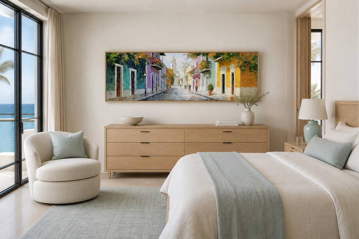 Long horizontal wall art of a colorful Old San Juan street scene above a wooden dresser in a bedroom.