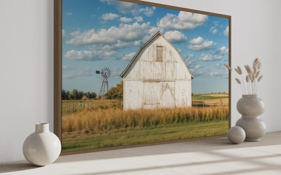 Framed canvas wall art of a weathered white barn and windmill in a golden field under a blue sky.