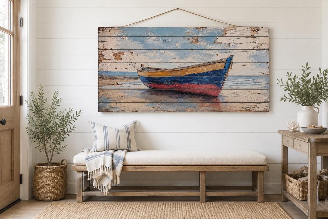 Distressed wood wall art of a weathered rowboat on a shore, hanging above a bench in a beach house.
