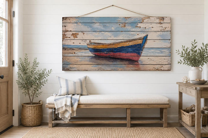 Distressed wood wall art of a weathered rowboat on a shore, hanging above a bench in a beach house.