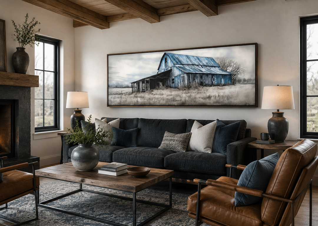 Long horizontal framed canvas wall art of a rustic blue barn in a living room setting.