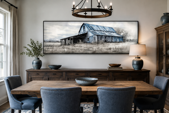 Old rustic blue barn painting on long horizontal framed canvas wall art in a dining room.