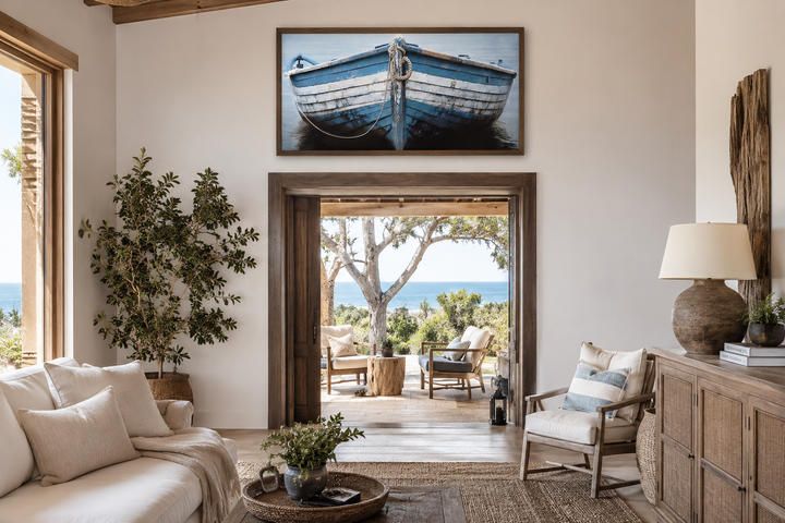 Rustic blue and white boat canvas print in a wooden frame above a doorway in a coastal living room.