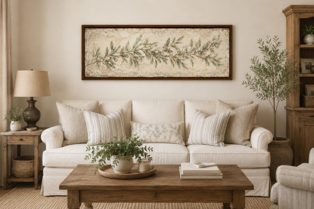 Long narrow canvas wall art featuring a sage green olive branch over a cream sofa in a living room.