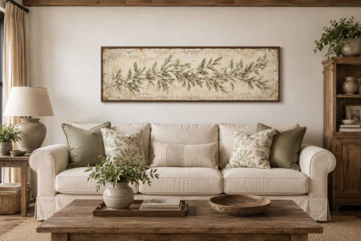 Long narrow canvas wall art featuring a sage green olive branch over a cream sofa in a living room.