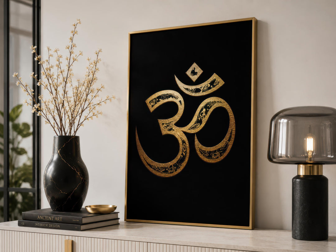 Gold and black Om symbol wall art displayed on a console table with a vase and lamp.