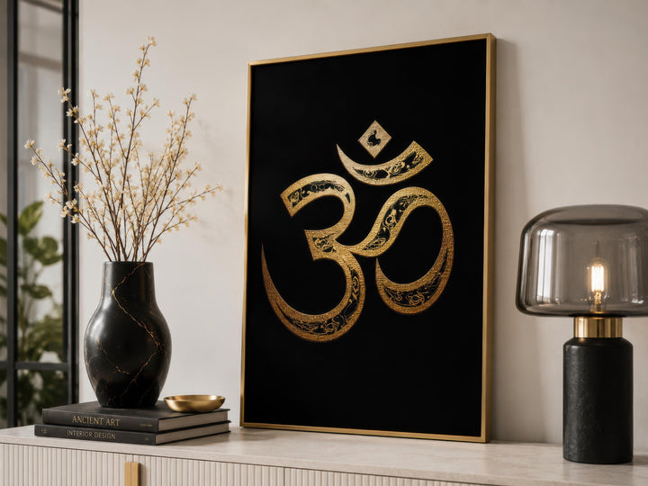 Gold and black Om symbol wall art displayed on a console table with a vase and lamp.