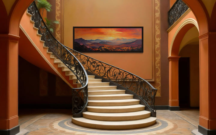 Horizontal framed canvas wall art of an orange mountain sunset hanging in a grand staircase hall.