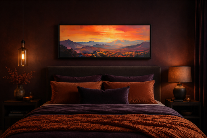 Horizontal framed canvas art of an orange mountain sunset hanging above a dark purple bed.
