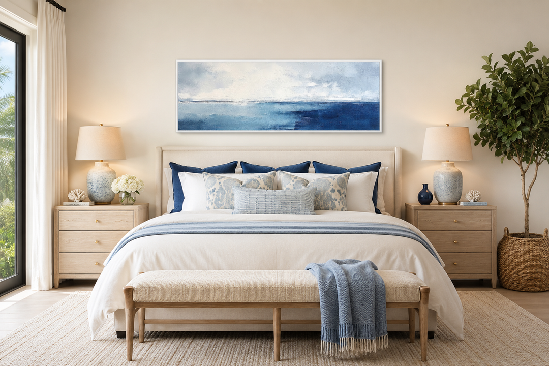 Minimalist panoramic ocean wall art in navy blue and grey framed above a bed in a coastal bedroom.