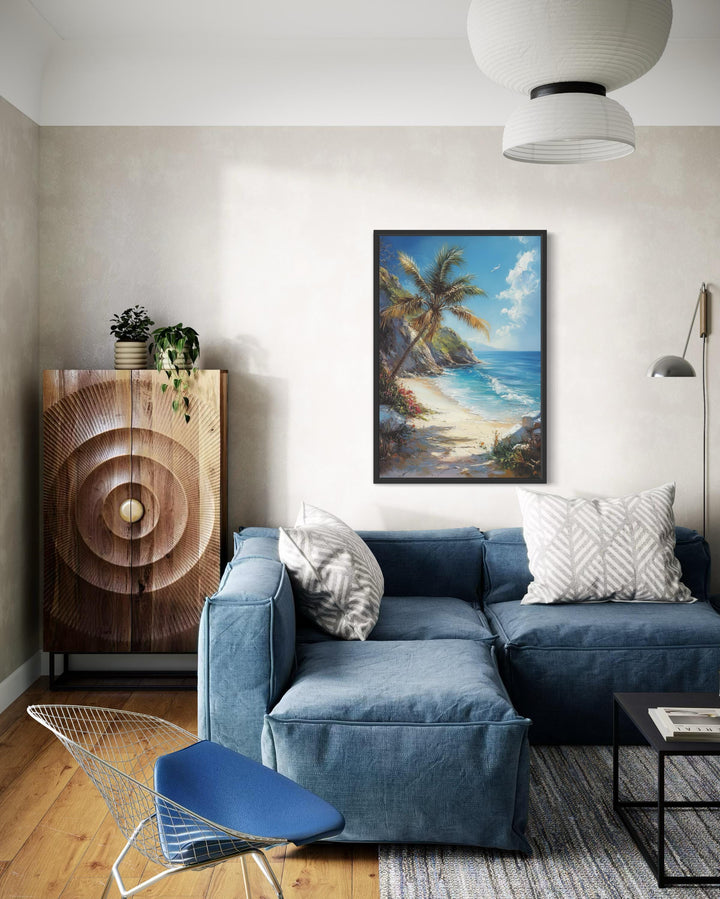 Palm tree with ocean view and tropical beach framed canvas wall art hanging above a blue sofa.