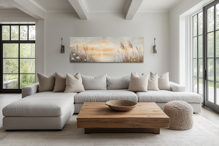 Horizontal canvas art of pampas grass on a beach at sunset, hung above a neutral sectional sofa.