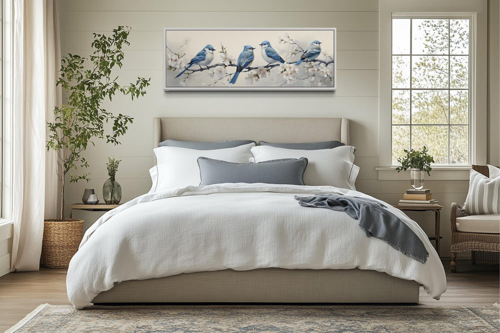 Panoramic watercolor wall art of blue birds on a branch, displayed above a bed in a neutral room.