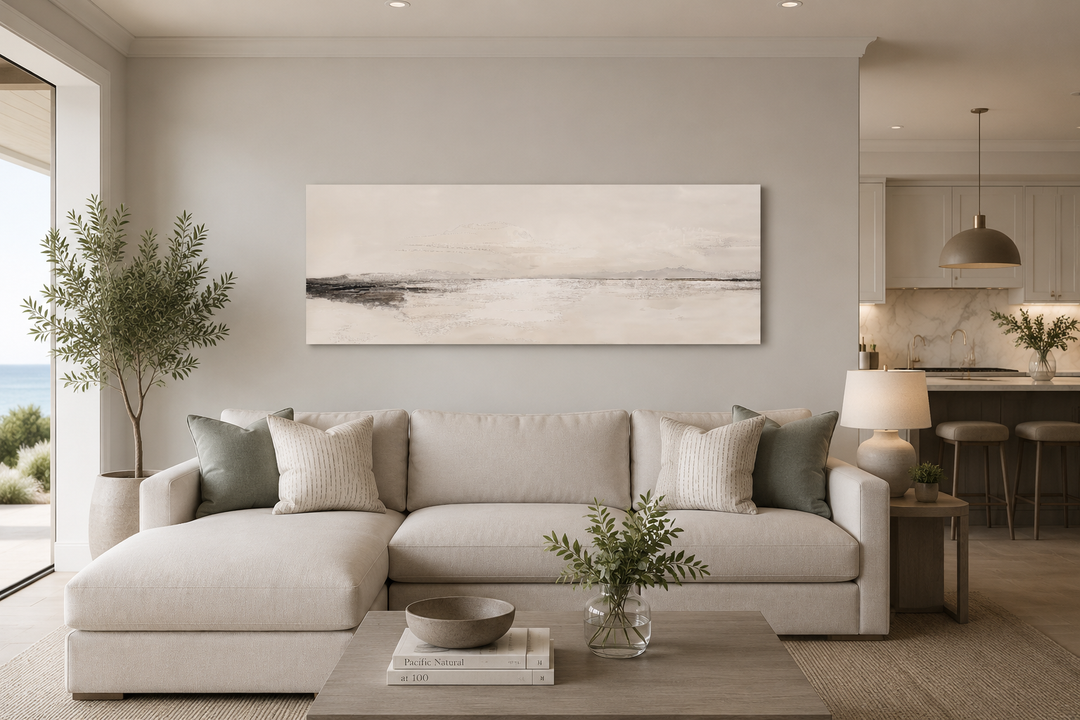 Panoramic coastal landscape framed canvas wall art in neutral tones hanging above a beige sofa.