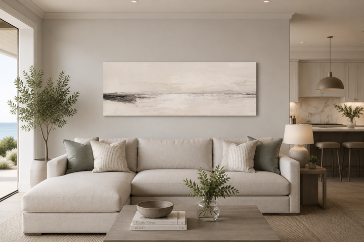 Panoramic coastal landscape framed canvas wall art in neutral tones hanging above a beige sofa.