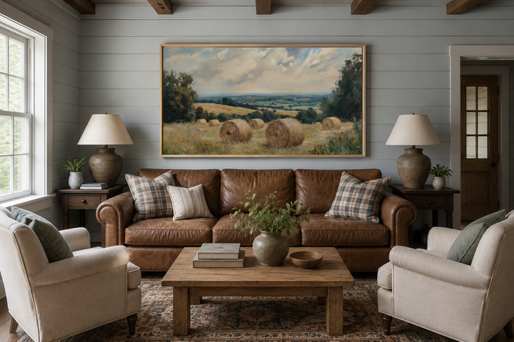 Pastoral hay field framed canvas wall art above a brown leather sofa in a farmhouse living room.