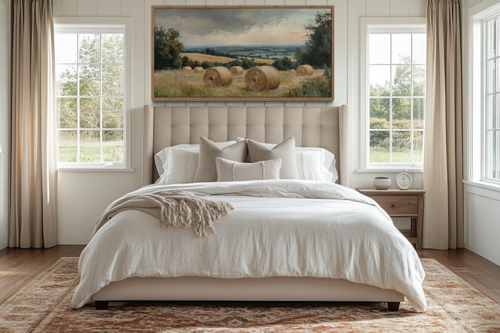 Pastoral hay field framed canvas wall art hanging above a bed in a farmhouse-style bedroom.