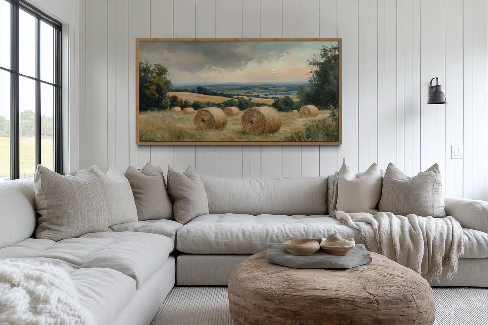 Pastoral hay field framed canvas wall art above a neutral sectional sofa in a farmhouse living room.