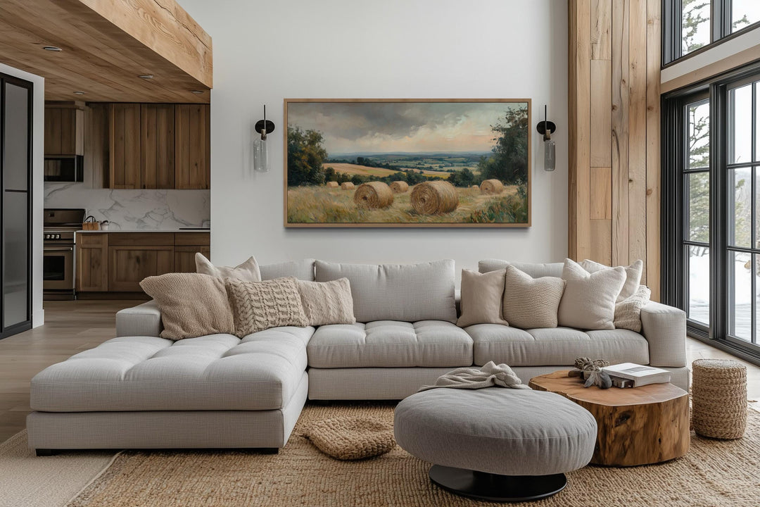 Pastoral hay field framed canvas wall art above a neutral sectional sofa in a farmhouse living room.