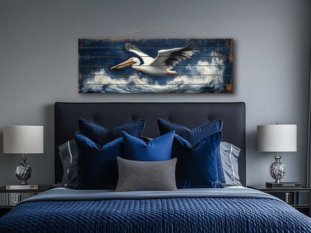 Pelican flying over ocean waves printed on long horizontal distressed wood wall art above a bed.