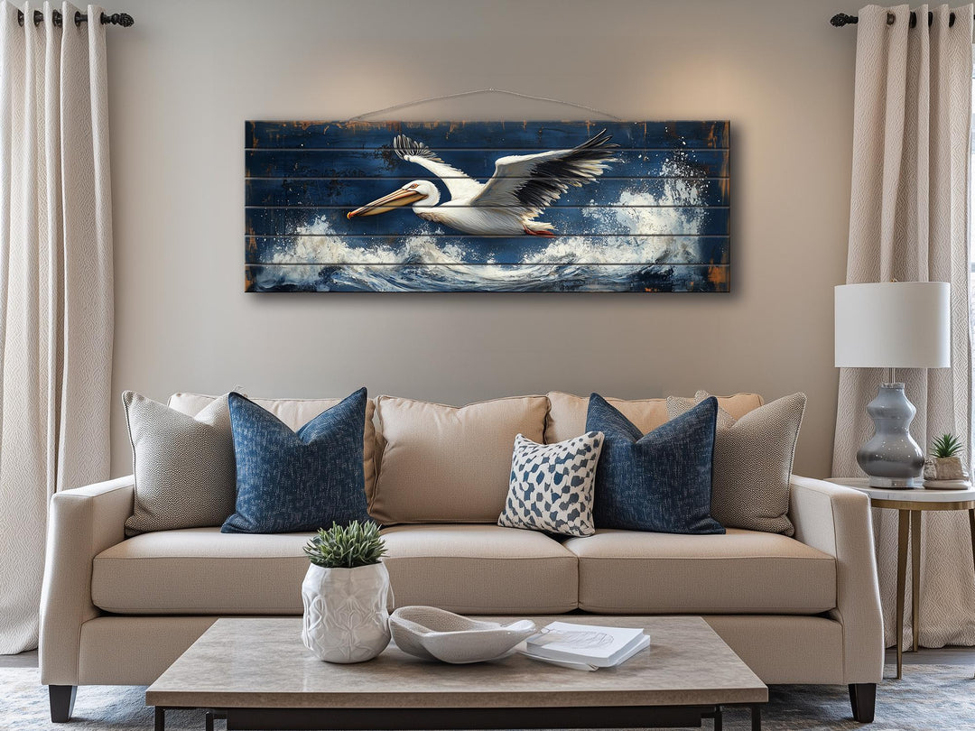 Horizontal nautical wall art of a pelican flying over ocean waves on distressed wood.