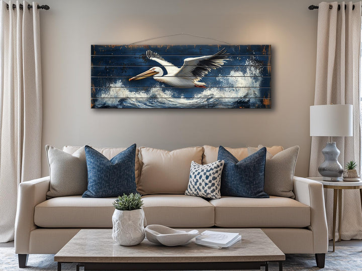 Horizontal nautical wall art of a pelican flying over ocean waves on distressed wood.