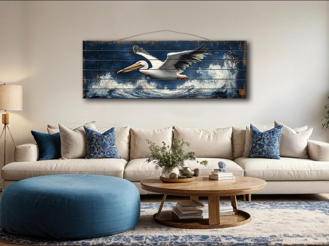 Horizontal nautical wall art of a pelican flying over ocean waves on distressed wood.