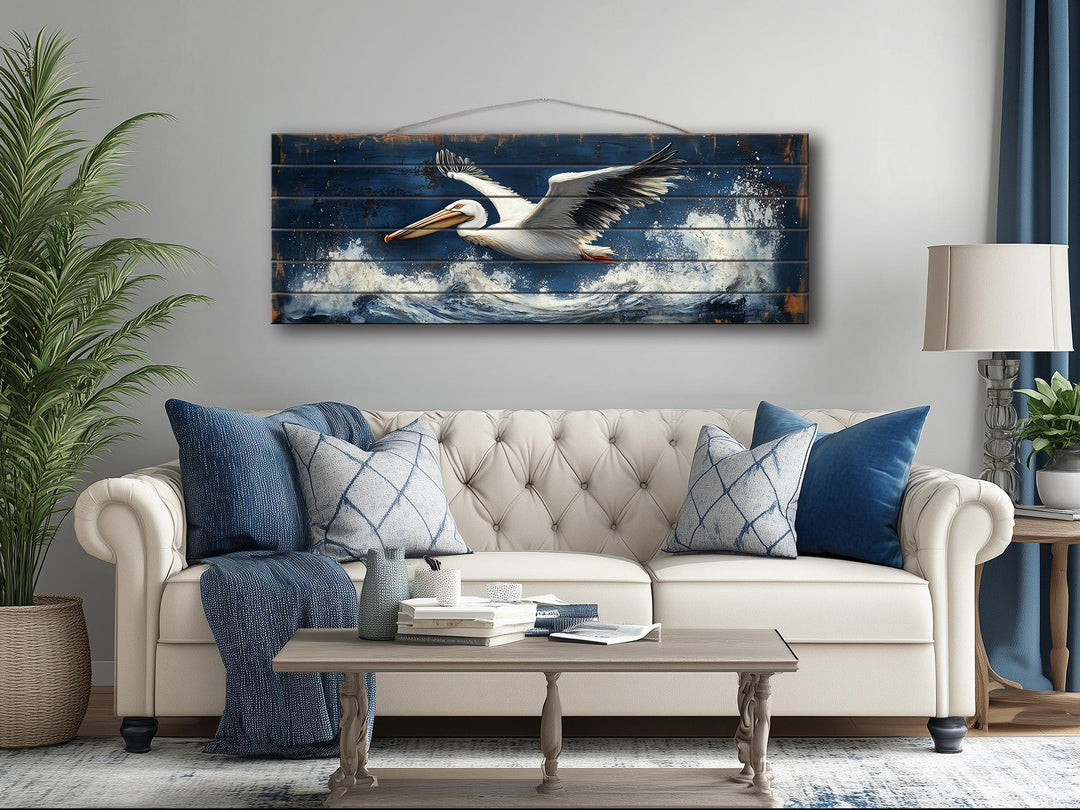 Horizontal nautical wall art of a pelican flying over ocean waves on distressed wood.