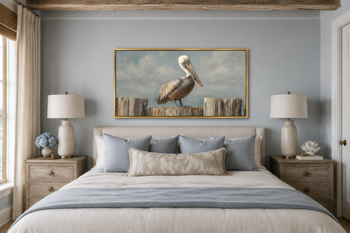 Pelican Standing On Wooden Posts Coastal Canvas Wall Art in a gold frame above a bed.