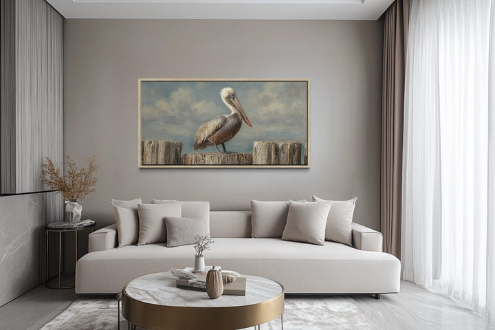 Horizontal coastal canvas wall art of a pelican on wooden posts above a modern neutral sofa.