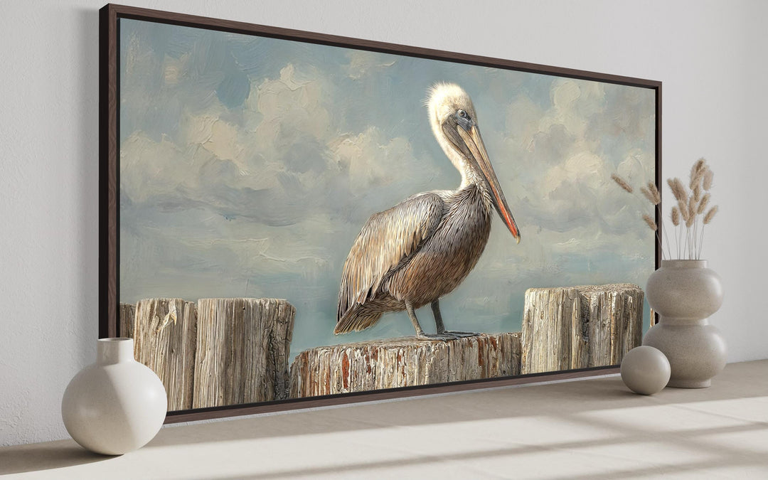 Pelican standing on wooden posts coastal canvas wall art in a dark brown frame.
