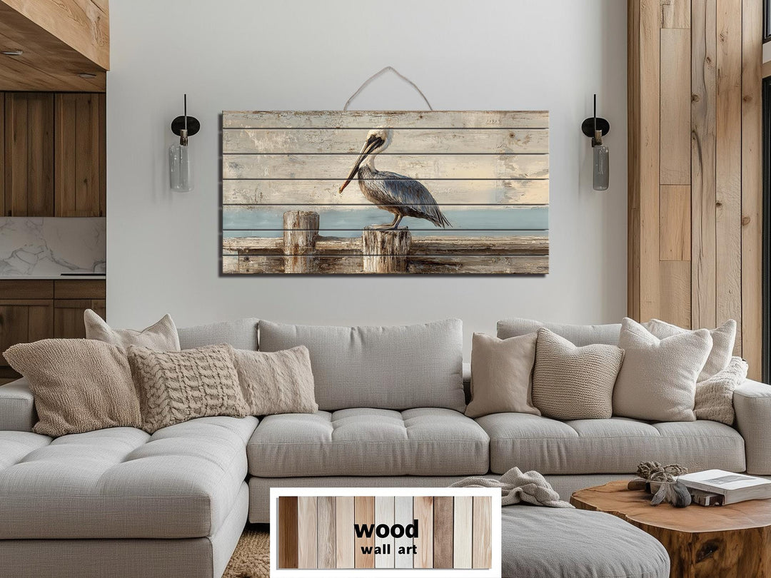 Pelican on a wooden dock coastal wall art printed on distressed wood planks above a gray sofa.
