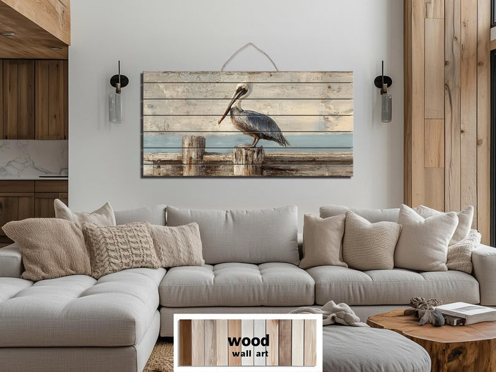 Pelican on a wooden dock coastal wall art printed on distressed wood planks above a gray sofa.