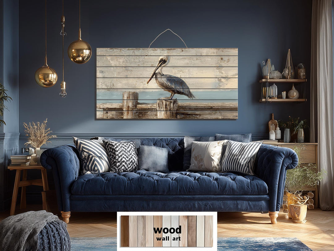 Pelican on standing on wooden dock distressed wood coastal wall art hanging above a blue sofa.