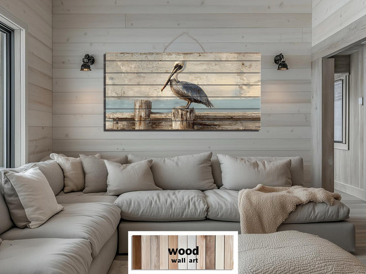 Pelican on a wooden dock coastal wall art printed on distressed wood planks above a neutral sofa.