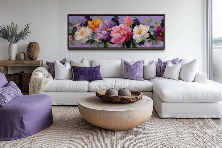 A long horizontal canvas print of vibrant purple and pink peonies hangs above a white sectional sofa.
