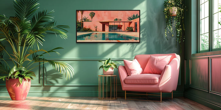 Framed mid-century modern wall art of a pink house and pool on a green wall above a pink armchair.
