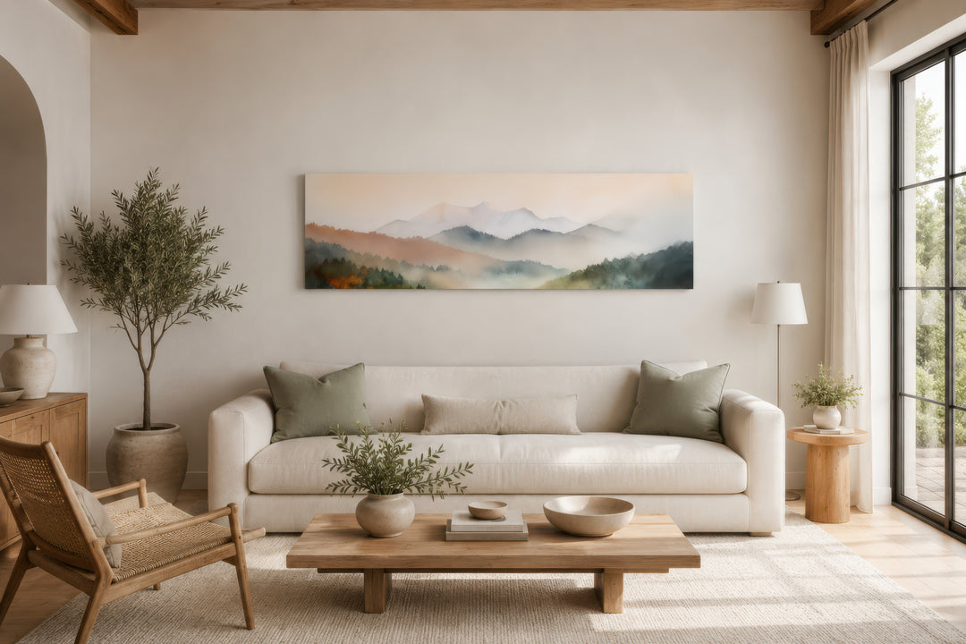 A wide canvas print of a pink and green pastel mountain landscape hangs above a white sofa.